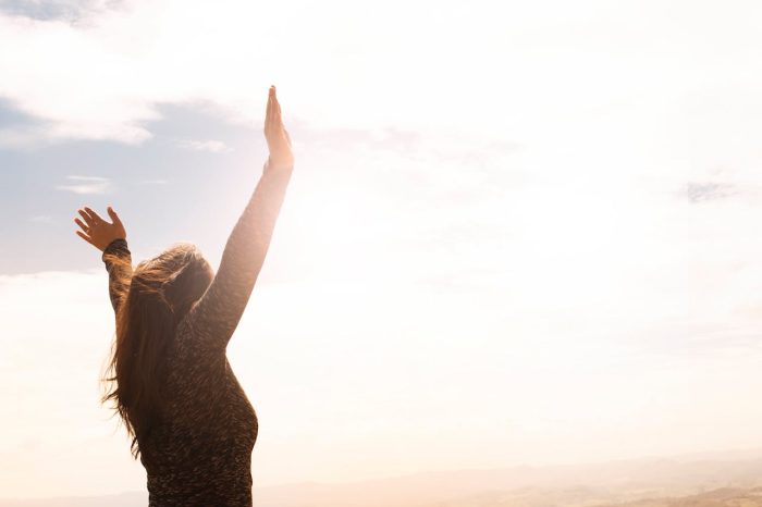 Frau mit erhobenen Händen vor sonnigem Himmel